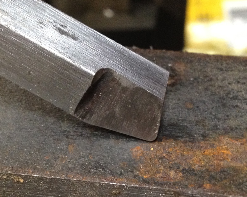 Metal tool with dark gray, brushed finish and curved cutting edge on a workbench.