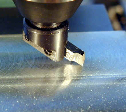 A close-up of a sharp fly cutter on a smooth metal work surface.