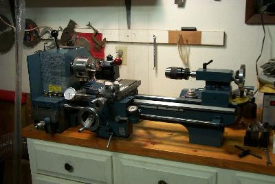 Lathe machine on wooden workbench with metal base and exposed interior.