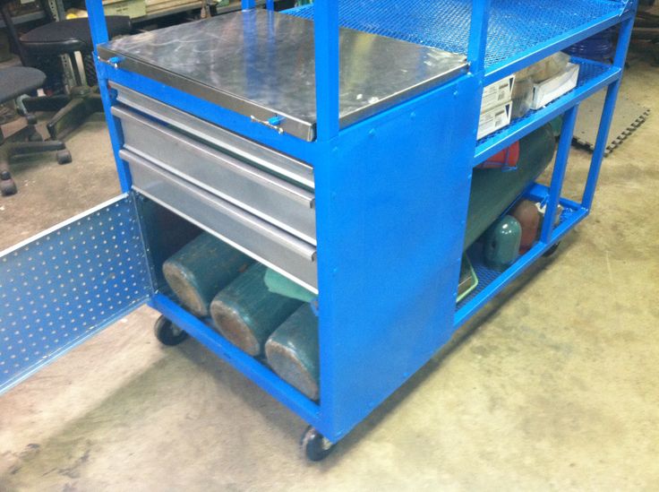 Blue metal cart with wheels and open door revealing a pegboard in a workshop or garage setting.