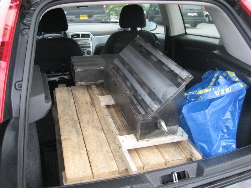 Compact car's trunk with wooden planks and a large black metal object on top in a parking lot/garage.