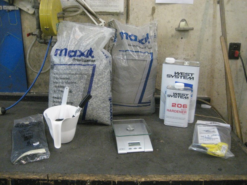 A cluttered workbench with various supplies and tools in a workshop or garage setting.