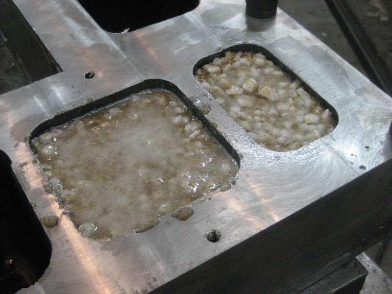 Metal workpiece with two recessed areas containing mixtures of particles and liquid.