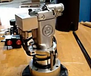 Silver machine part with cylindrical base and square top on wooden surface.