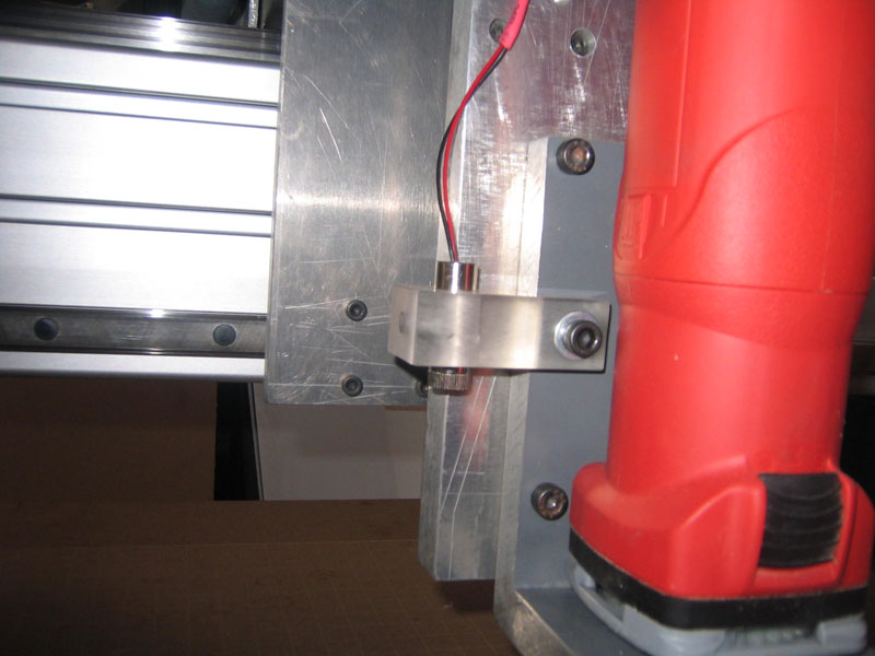Red cylindrical object attached to aluminum bracket with screws.