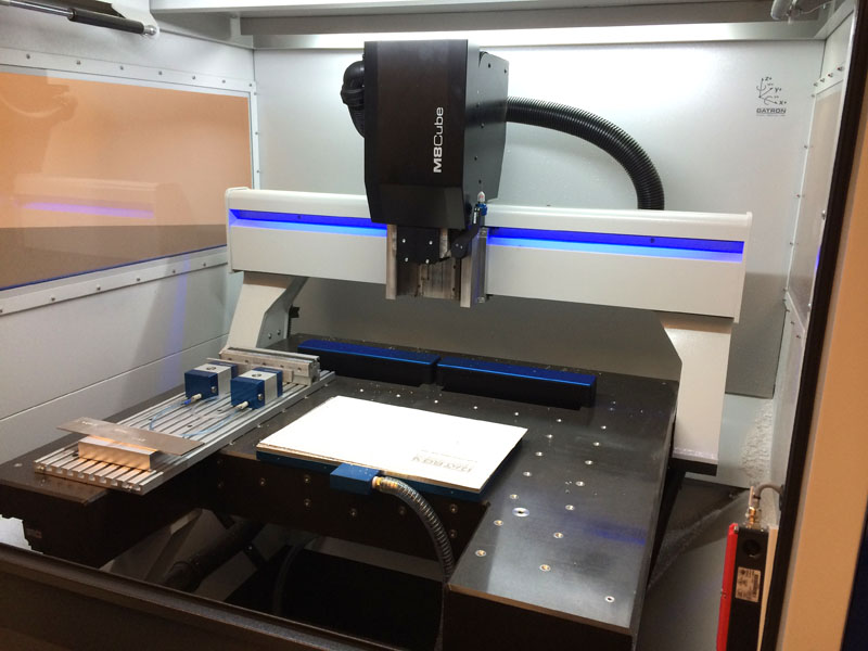 Industrial-sized machine with black arm and white body, featuring blue lights in a commercial workshop.