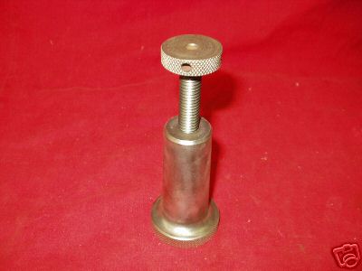 A small, cylindrical metal object with a threaded end and knurled surface on a red background.