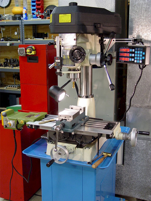 Micro milling machine with black lid and yellow warning labels, situated in a workshop or garage with various tools and equipment visible in the background.