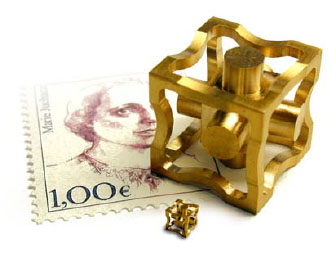 Gold-colored metal cube with wavy edge and cylindrical protrusion on a French Marie Antoinette postage stamp.