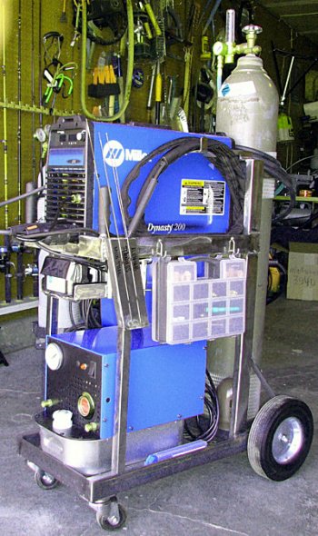 Blue welding cart with a Miller Dynasty 200 welding machine and various metalworking tools.