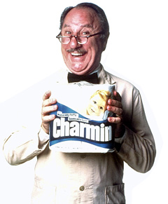Man with mustache and glasses holding a box of Charmin toilet paper.