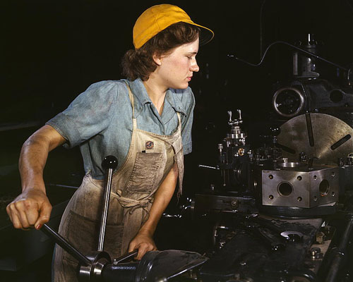 Woman in overalls operating machinery in a workshop.