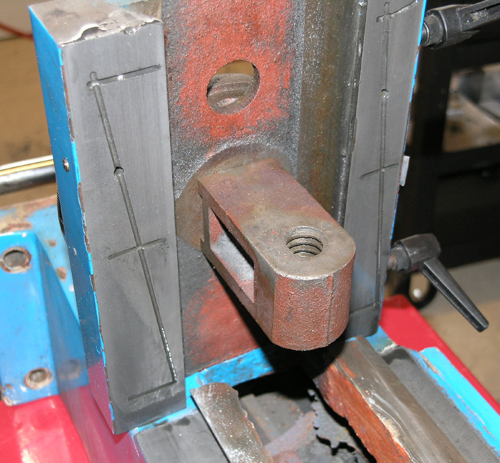 A worn, rusted metal tool or component with a hole and lever.