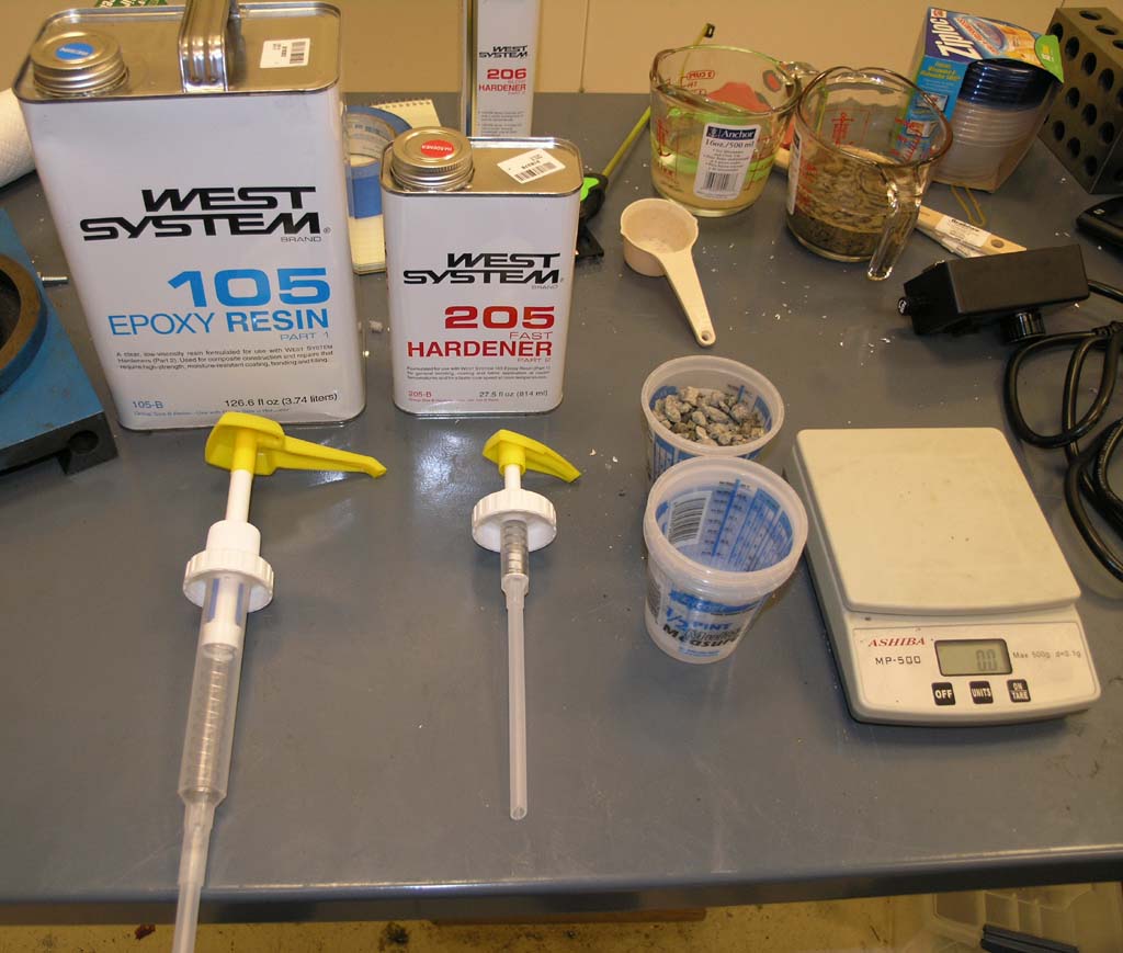 Cluttered workshop countertop with epoxy resin containers, metal scale, and various tools.