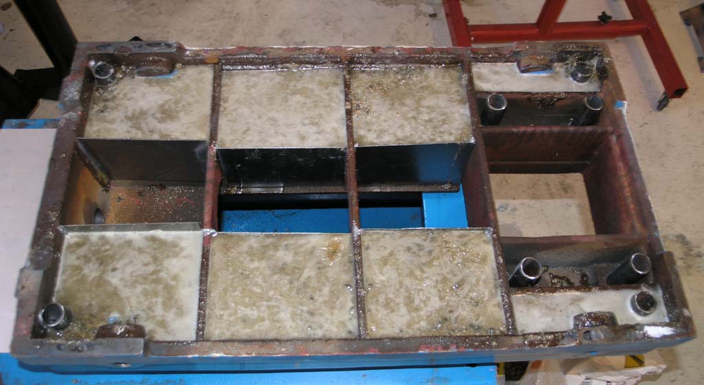 Metal mold with grid-like pattern on dark-colored metal work surface in a workshop.