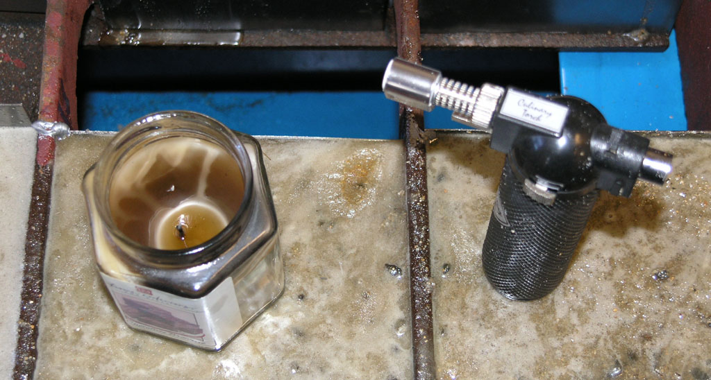 Candle and tool on metal surface near CNC machine equipment.