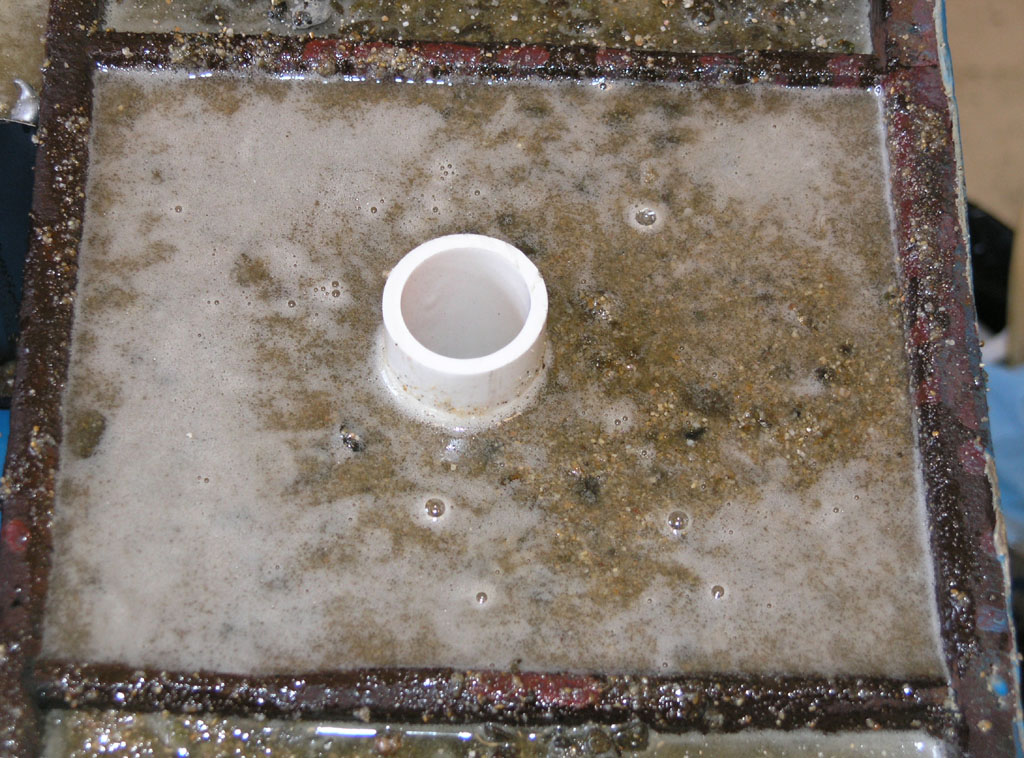 Dirty industrial metal part with white pipe fitting.