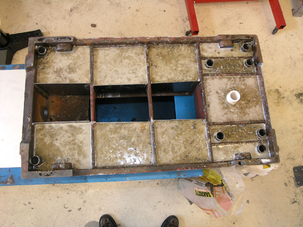 A large metal object with a rectangular shape and square openings, sitting on a concrete floor, made of rough steel-like material.