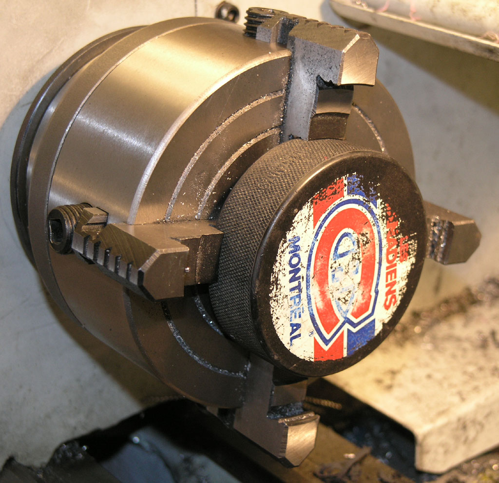 A hockey puck with Montreal Canadiens logo mounted in a lathe chuck for machining.