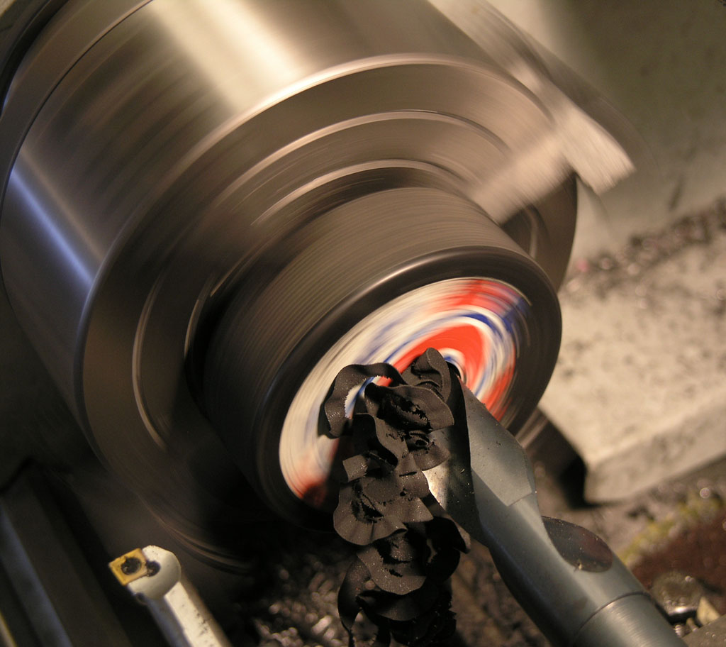 Large metal lathe with red, white, and blue workpiece being turned on axis.