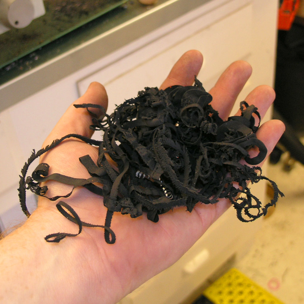 Black rubber shavings on hand against industrial background.