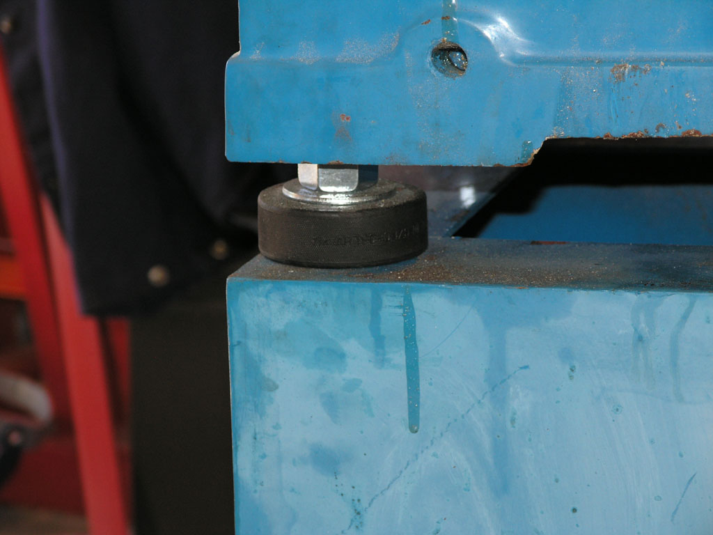 Blue metal object with attached black rubber wheel in industrial workshop setting.