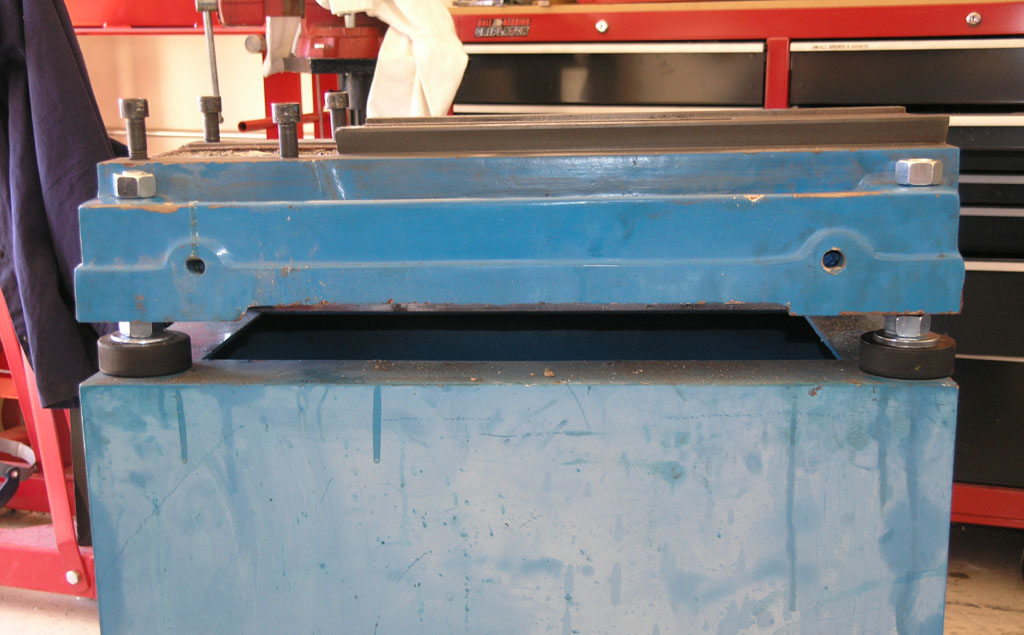 Blue metal box with rectangular opening and black rubber wheels in a workshop setting.