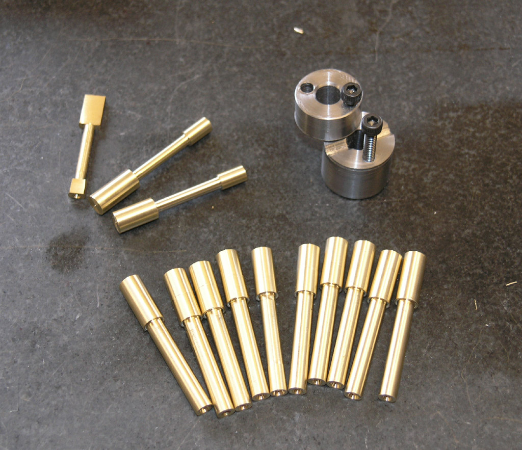 Precision metal parts on dark gray surface, including brass dowel pins and metal components.
