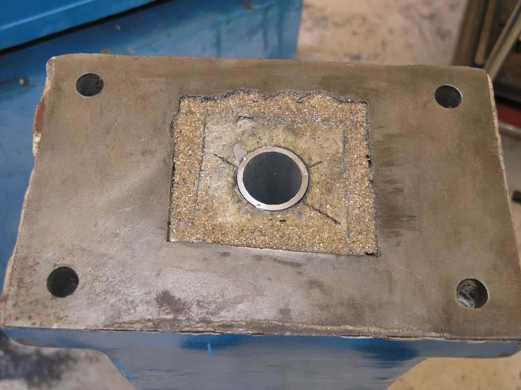 Metal object with circular hole and four corner holes, textured metal surface.