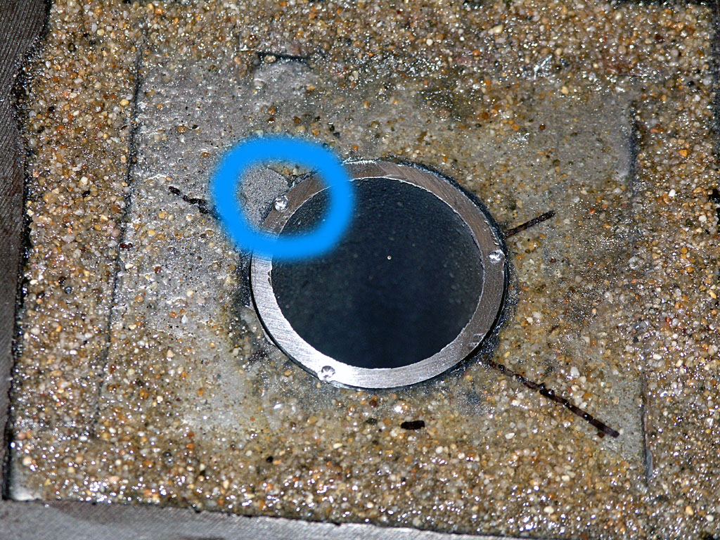 Circular metal object with black center and silver ring embedded in concrete surface.