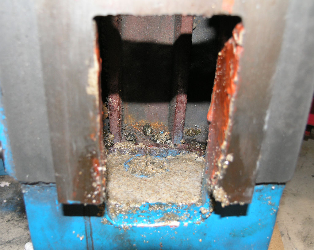 Industrial workshop with large metal object at an angle featuring a rectangular opening to its interior, containing a blue-colored metallic component with rough texture.