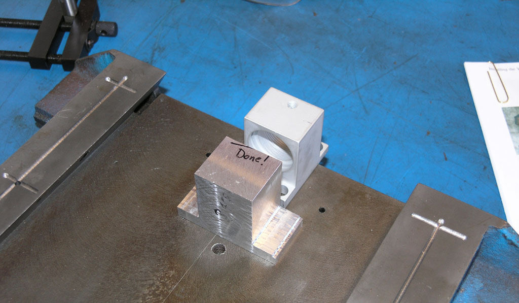 Two machined aluminum blocks on a blue workbench.