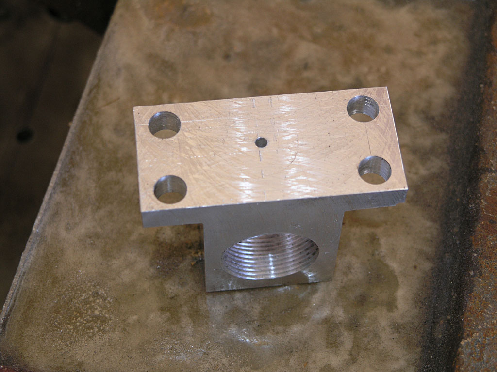 Silver metal piece with evenly spaced holes and threaded hole on concrete surface.