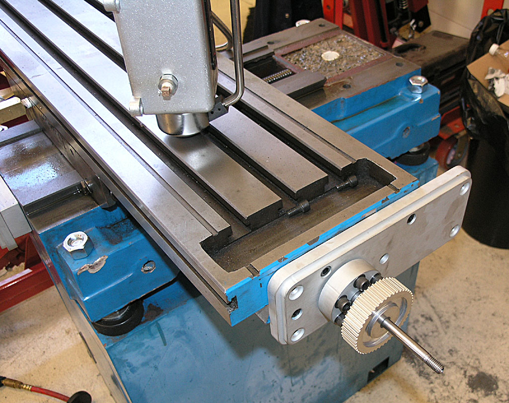Blue and silver metalworking machine with tools and parts on a flat surface.