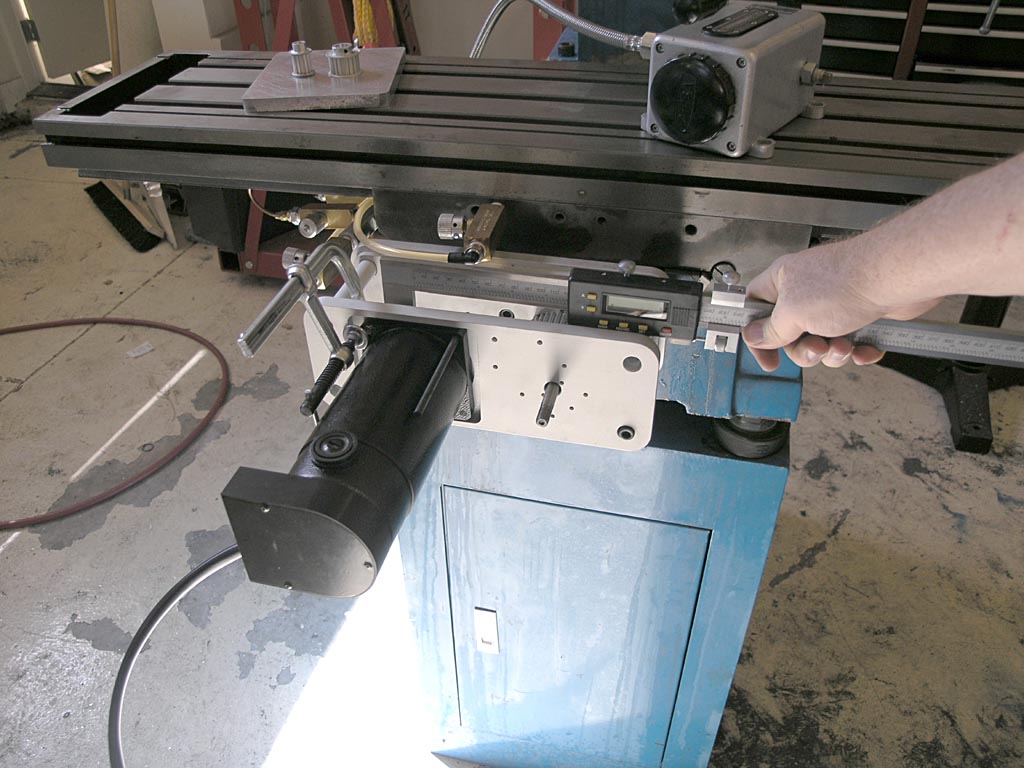 Person operating a milling machine in a workshop with digital display screen, red hose, and cluttered background.