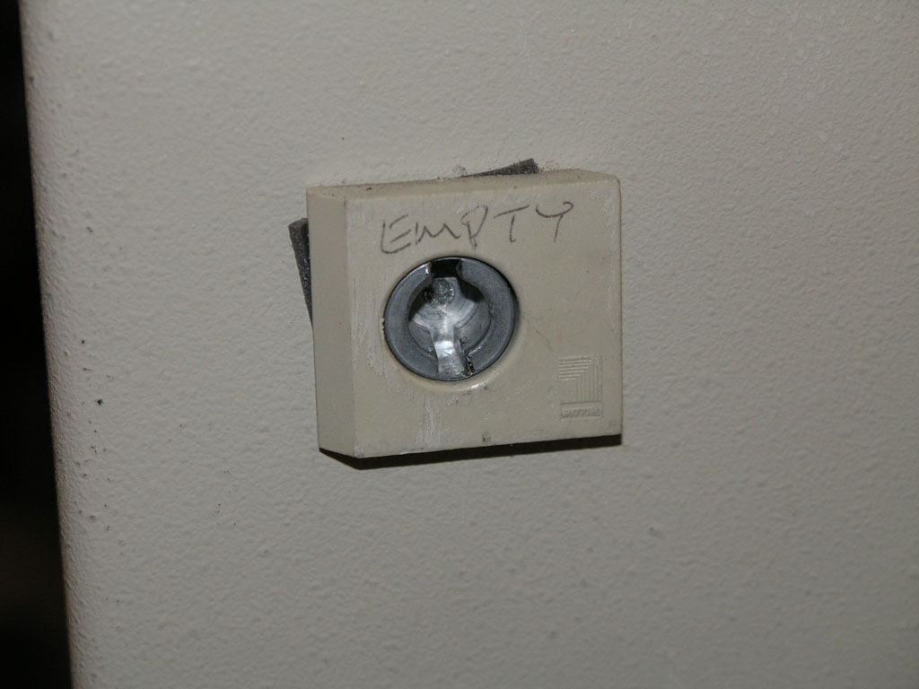 Beige electrical box with silver metal piece on off-white wall, handwritten "EMPTY" above.