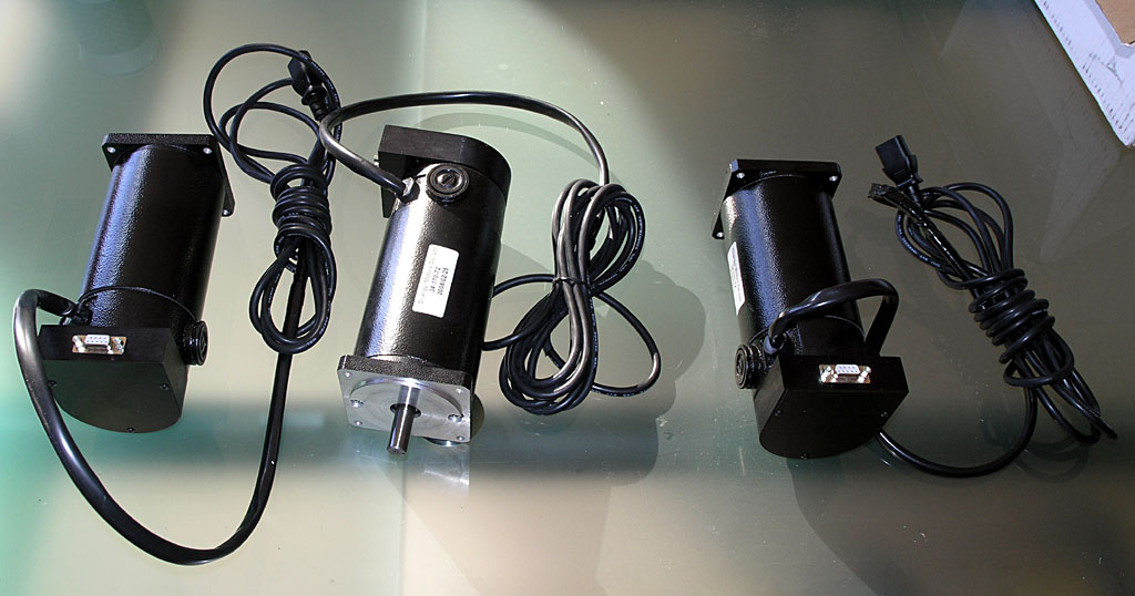 Two black electrical motors with cords on a reflective surface.