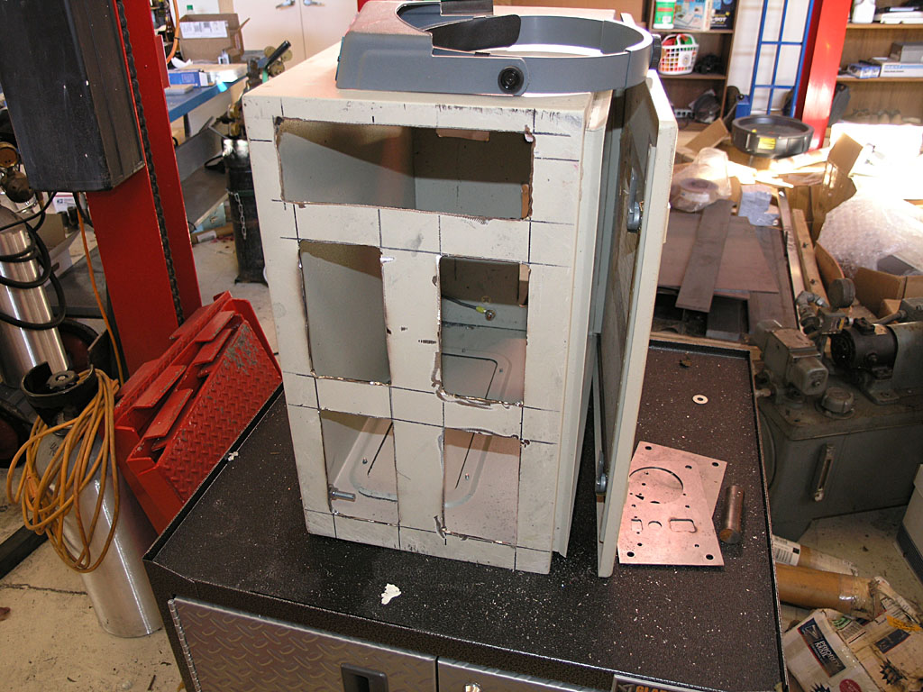 A gray metal component on a black toolbox in a cluttered workshop with various tools and machinery parts.