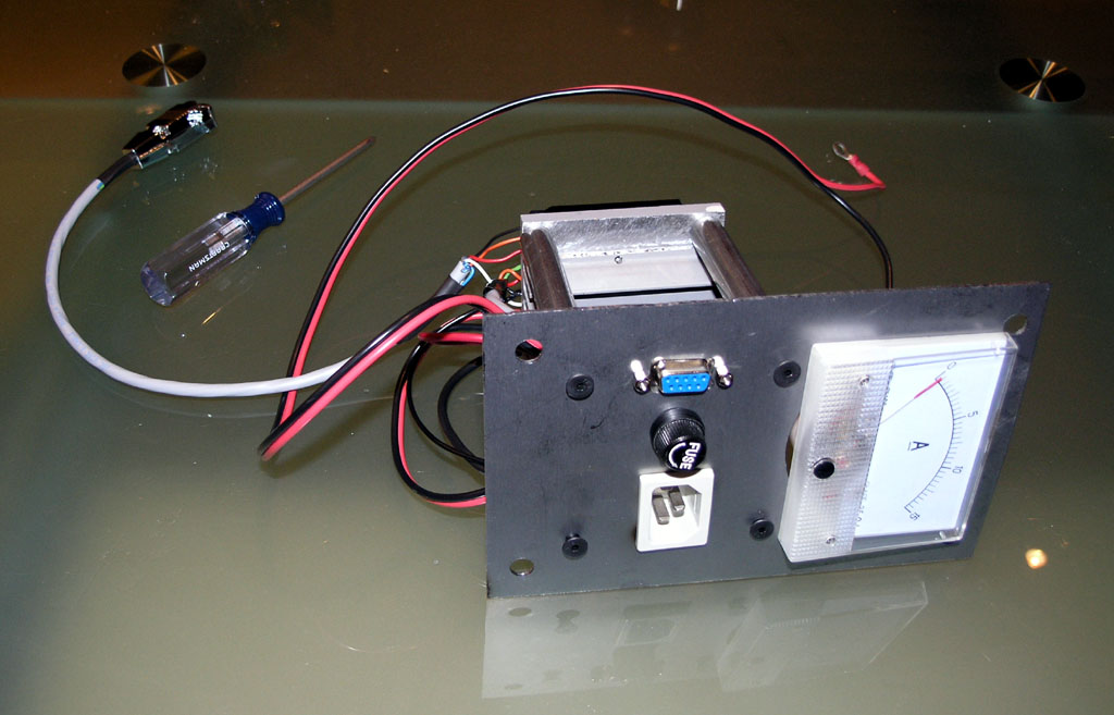 Metal box with components attached, including dial gauge and knobs on a workbench.