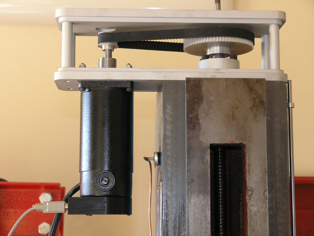 Large metal machine with gears, levers, and black cylinder, situated on off-white background.