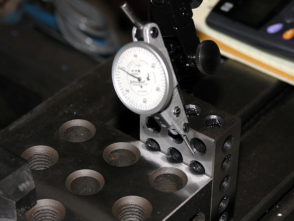 Dial test indicator on a stand over a metal surface with numerous holes.