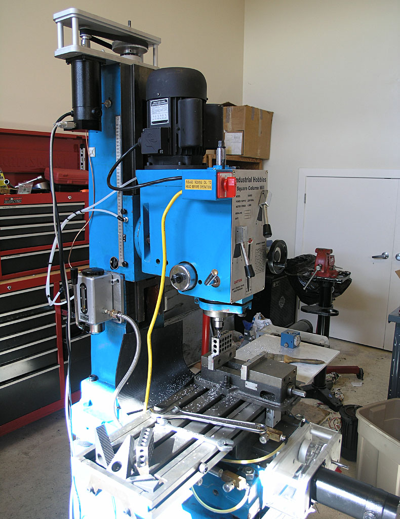 Blue industrial milling machine with attachments and tools in a well-lit workshop.