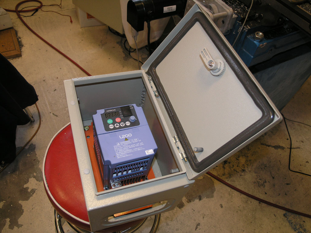 A small gray metal box with digital display and controls, containing a blue motor, on a red stool.