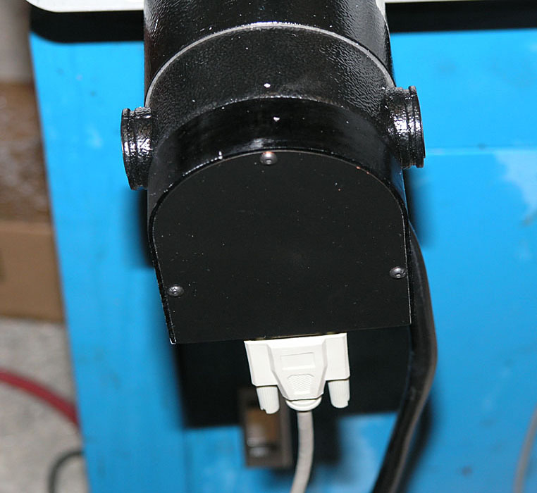 Black metal pipe with white electrical outlet attached, on a workshop or garage background.