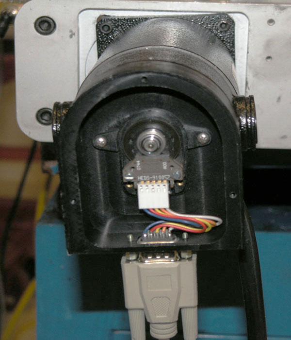 Industrial camera with black plastic casing and circular opening, on a workbench.