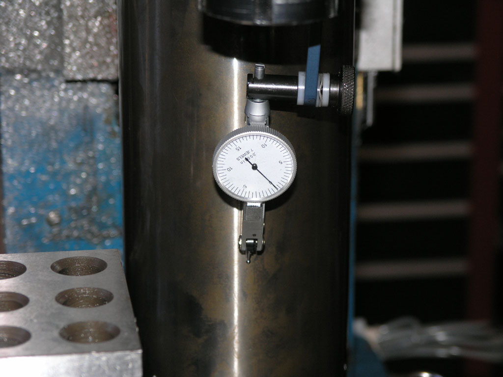 A dial test indicator mounted on a cylindrical metal object with holes.