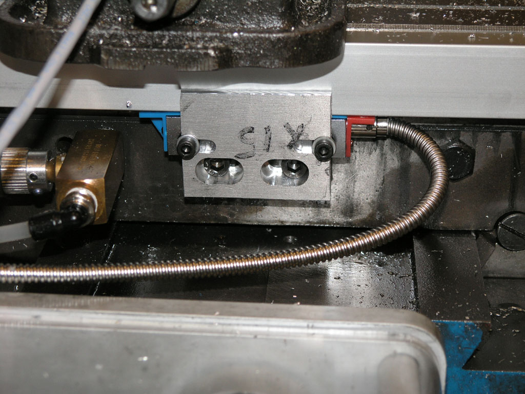 Metalworking machine's internal components, including rectangular piece of metal with three circular holes and the engraved lettering "SIX".