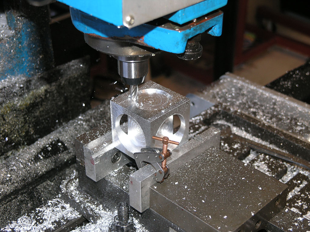 A close-up view of a drilling or milling machine working on an aluminum part with multiple holes, using a drill bit or end mill.