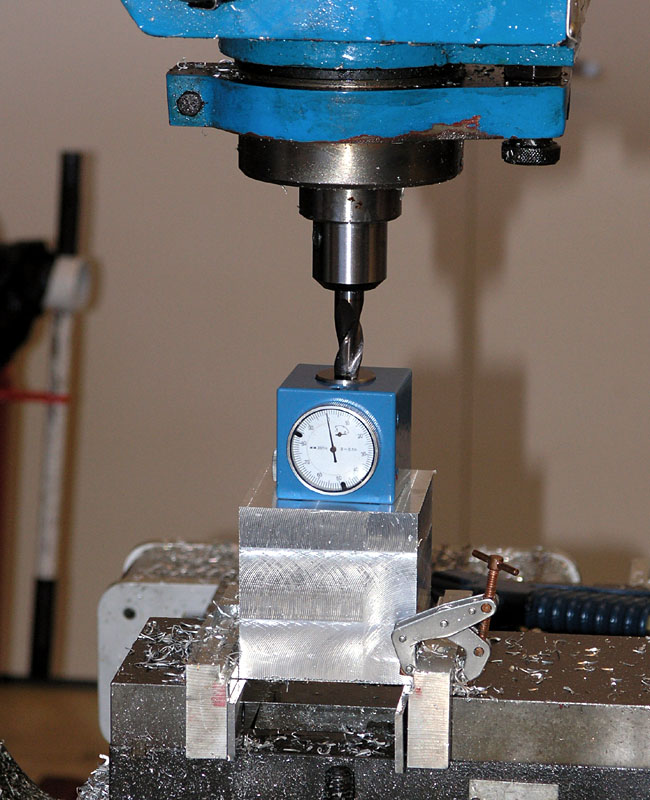 Blue drill press with depth stop gauge attached, situated on a metal table.