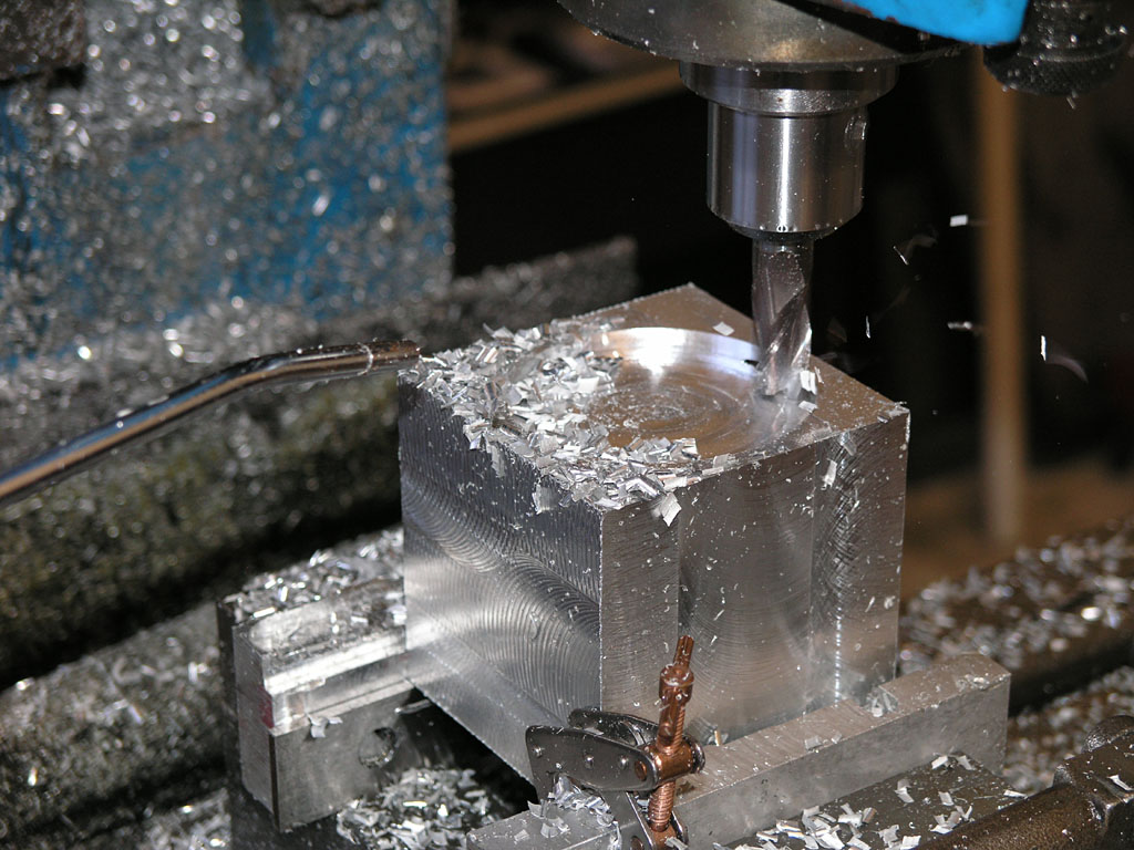 Metalworking machine with drill bit or end mill cutting through metal block.